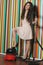 Portrait of young woman with vacuum cleaner standing against colorful striped wall