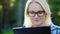 Portrait of a young woman wearing glasses, enjoying a tablet pc in the park. Beautiful sun glare