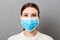 Portrait of young woman wearing medical mask at gray cement background. Person is happy because she is finally healthy. Protect
