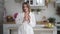 Portrait of young woman in white bathrobe drinks coffee or tea in kitchen