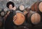 Portrait of a young woman winemaker standing with a glass with wooden barrel of red wine in a winery cellar or