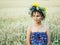 Portrait of a young woman in a wreath of wild flowers stands in the field at sunset.