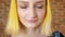 Portrait of young woman with yellow hair opens eyes, brick wall background, model with unusual hairstyle with closed