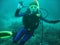 The portrait of young women scuba diver under water. She is in full scuba diving equipment: mask, regulator, BCD. She is showing O