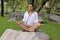 Portrait of young yogi man in white shirt doing yoga meditation while sitting in lotus position on the rock in beautiful outdoor p