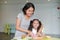 Portraits Asian mother and daughter slicing cucumber vegetable on chopping board at play room. Mother teaches her little child