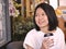 Portraits of Asian woman holding a cup of coffee looking to her right hand in cozy coffee shop.