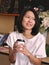 Portraits of Asian woman holding a cup of coffee by two hands looking to her left hand in cozy coffee shop.