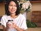 Portraits of Asian woman holding a cup of coffee by two hands looking to her left hand in cozy coffee shop.