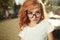 Portraits of a charming red-haired girl with a cute face. Girl posing for the camera in the city center. She has a wonderful mood