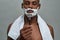 Portrat of focused naked african american man with face in shaving foam holding razor, posing isolated over gray