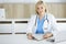Portrate of woman-doctor at work while sitting at the desk in clinic. Blonde cheerful physician filling up medical form
