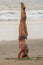 Pose Shirshasana. A young woman in a bikini is engaged in yoga on the beach.