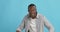 Positive african american guy dancing, blue studio background