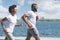 Positive Afro Couple Jogging Along River Embankment In City