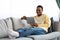 Positive black man reclining on sofa, using digital tablet