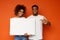 Positive black man and woman pointing at white empty board