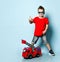 Positive blond boy in bright stylish casual clothing, sneakers, sunglasses standing near toy fire engine and showing thumb sign