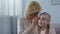 Positive blond grandmother whispering secret to surprised granddaughter, family