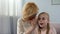 Positive blond grandmother whispering secret to surprised granddaughter, family