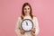 Positive blond woman holding big wall clock, looking at camera with pleasant smile, time to go.