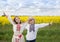 Positive boy and girl 6-7 years old in national Ukrainian clothes are standing in front of yellow rapeseed field
