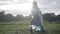 Positive boy and girl in raincoats spinning in sunlight outdoors on rainy summer day. Wide shot of cheerful Caucasian