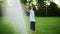 Positive boy standing in meadow. Child playing with water sprinkler in field