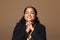 Positive brazilian plus size woman dreaming and doing pray gesture with hands, making a wish, brown background