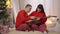 Positive caring man teaching pregnant woman playing guitar on New Year's eve at home. Wide shot of smiling loving