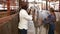 Positive Caucasian girl and afro man using electric trimmer for shearing gray horse in stable