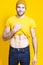 Positive Caucasian Handsome Man In Yellow Tshirt Posing in Warm Hat Over Yellow Background While Pulling Shirt Off