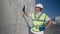 Positive Caucasian man in uniform and hard hat touching huge stack of packed industrial products smiling. Portrait of