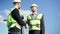 Positive Caucasian men in hard hats and uniform shaking hands at background of clear sky outdoors. Handshake of