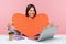 Positive cheerful woman holding big red paper heart talking on video call on laptop sitting at workplace, romantic date online