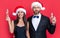 positive christmas couple in santa hat hold champagne isolated on red. corporate christmas