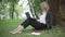 Positive confident businesswoman messaging online on laptop sitting on green summer lawn in park. Wide shot portrait of