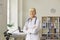 Positive confident elderly woman doctor in uniform standing and looking at camera