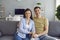 A positive couple embracing looking at the camera while sitting on a sofa in the interior room of the house.