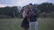 Positive couple standing on windy summer meadow in the evening and using smartphone. Portrait of creative Caucasian