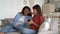 Positive curious mother with laptop and shy teenage girl with mobile phone sits on sofa in home