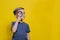 Positive curious schoolboy in casual clothes looking at camera through magnifying glass while standing on yellow background. Copy