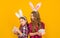 positive easter children in bunny ears hold gift box on yellow background