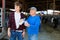 Positive elderly dairy farm owner with teenage grandson tasting fresh milk in cowshed