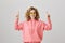 Positive emotive girl in trendy yellow sunglasses and pink hoodie pointing up with raised index fingers, being excited