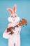 Positive funny musician guitarist plays music by ukulele or Hawaiian guitar isolated on blue. Easter bunny or rabbit or