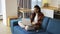 Positive girl with dreadlocks sitting on sofa with laptop on knees