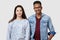 Positive girl and guy of different races poses against white studio wall, smile positively, express their happiness, dressed in