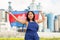 Positive girl in overalls with the Cambodia flag in her hands against the background of chimneys of modern factory