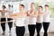 Positive girl with women and men engaged in group class perform exercise near ballet barre,